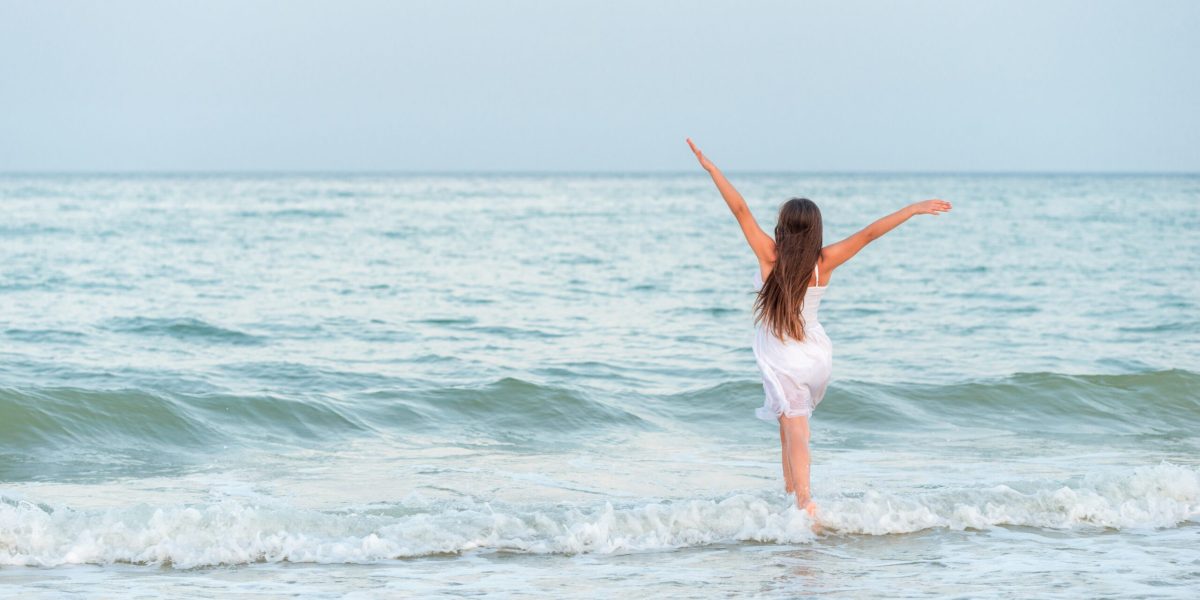 Girl happily spends time on the beach and walks along the sea waves on a sunny summer evening during vacation.